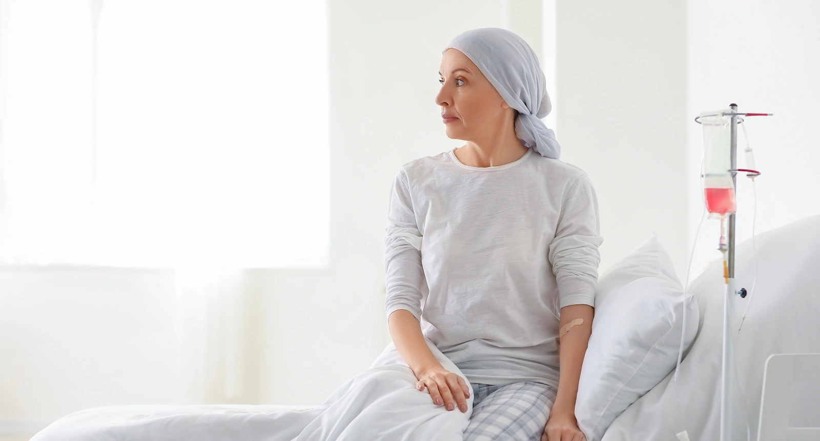 A woman looks out the window sitting on a hospital bed