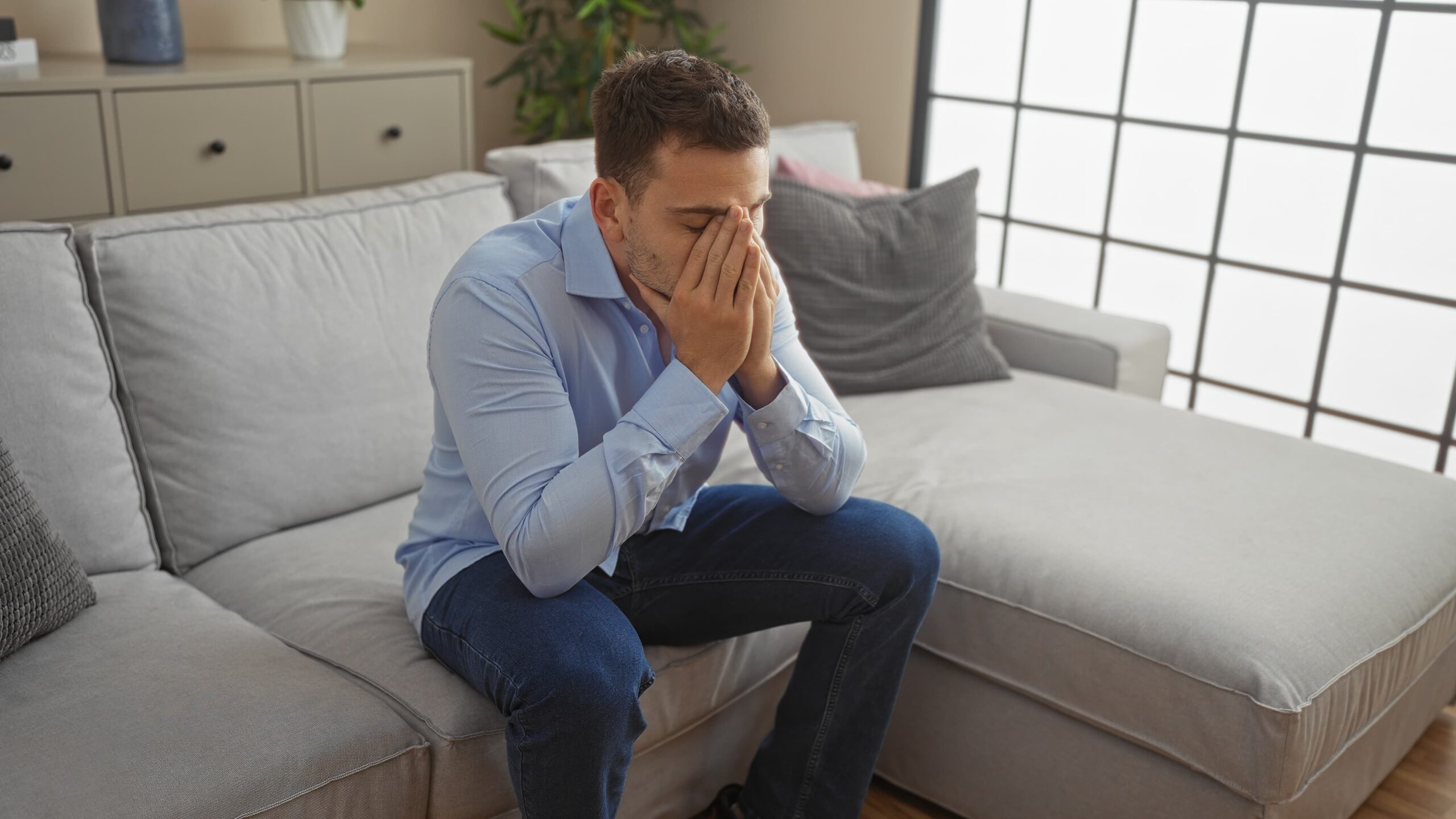 A man sits at the edge of his seat stressed about something with his hands over his mouth
