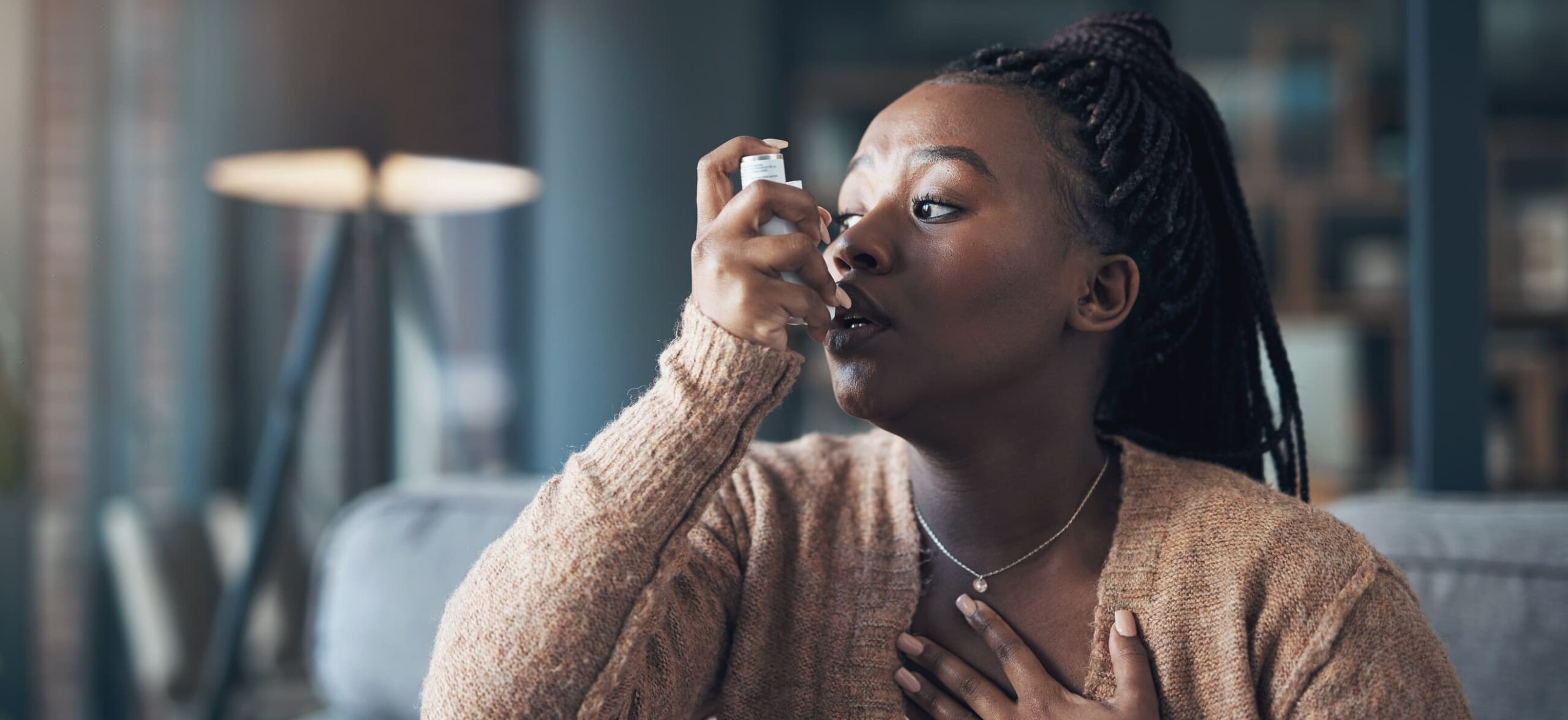A woman takes an inhaler as she holds her chest with her other hand