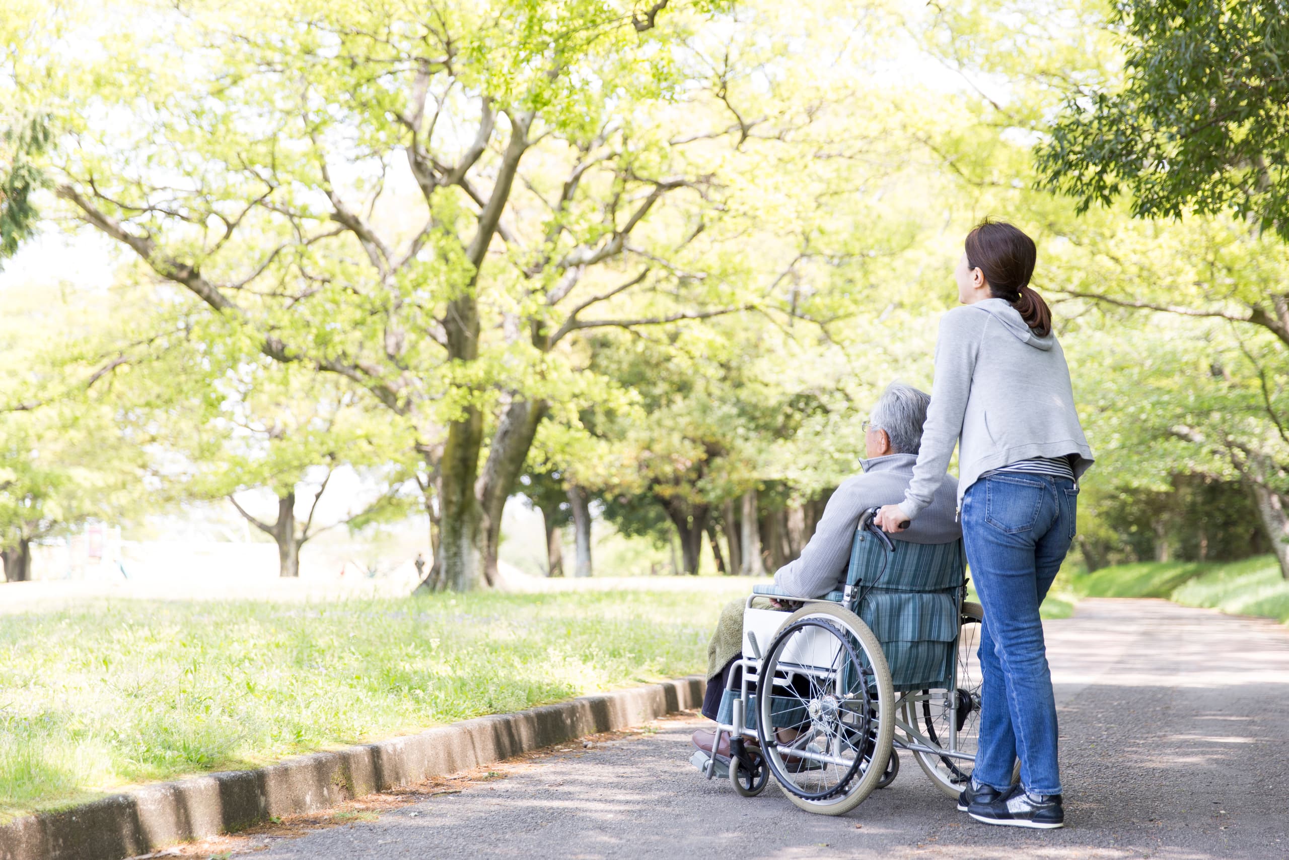 A woman pushes an older man in a wheelchair in a park