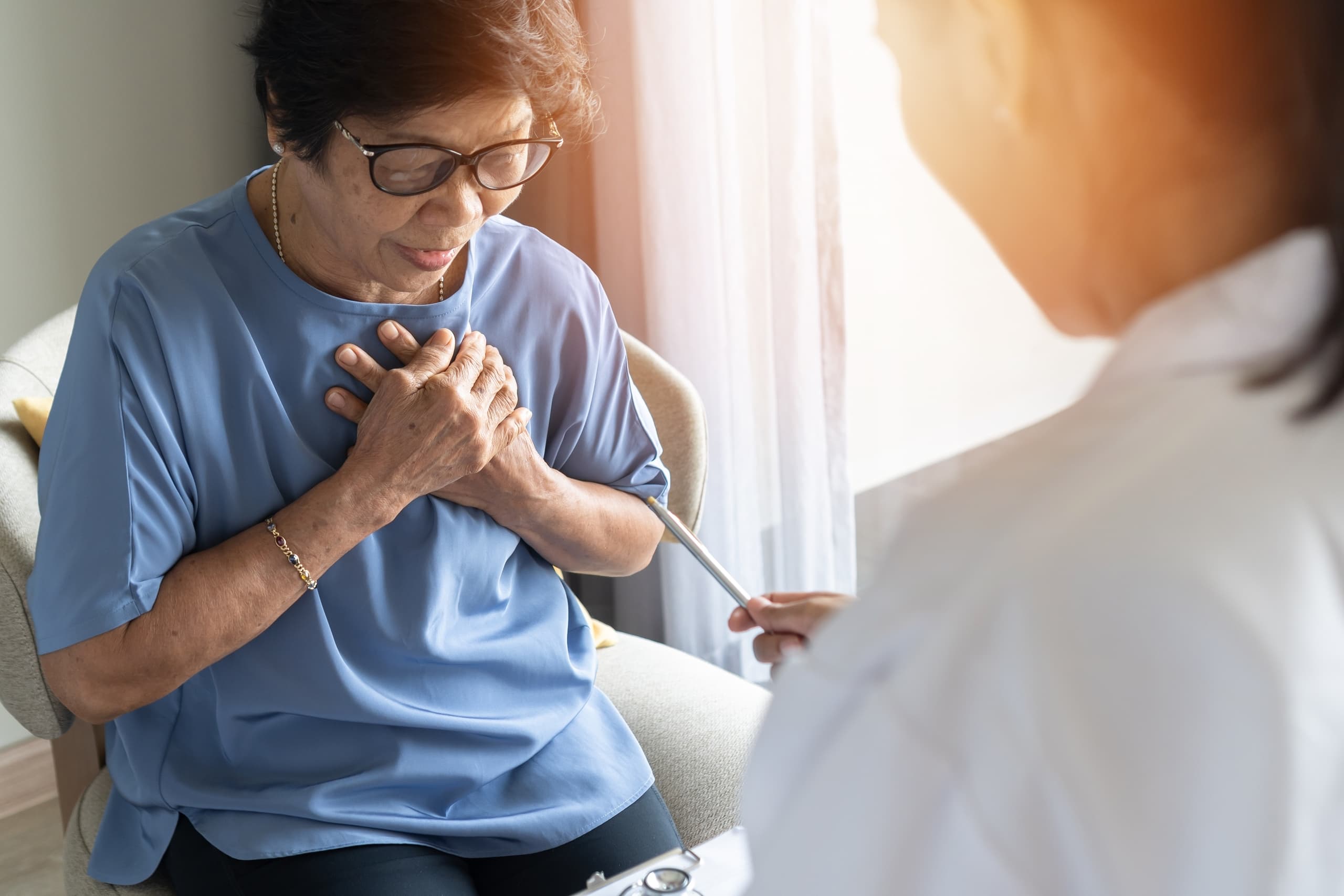 A woman clasps her hands on her chest over her heart while talking to a medical professional