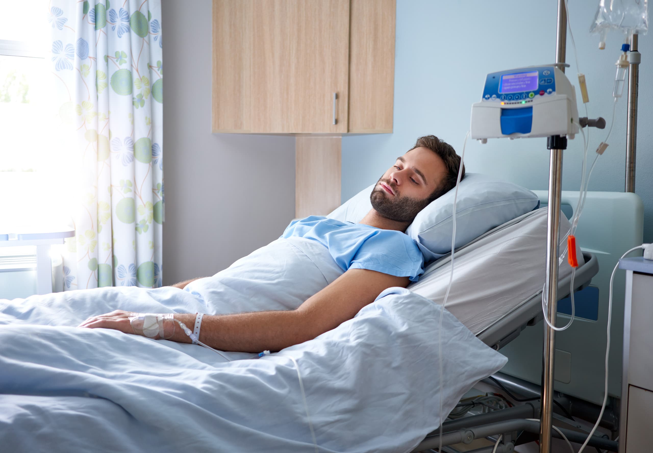 A man lays in his hospital bed looking sad