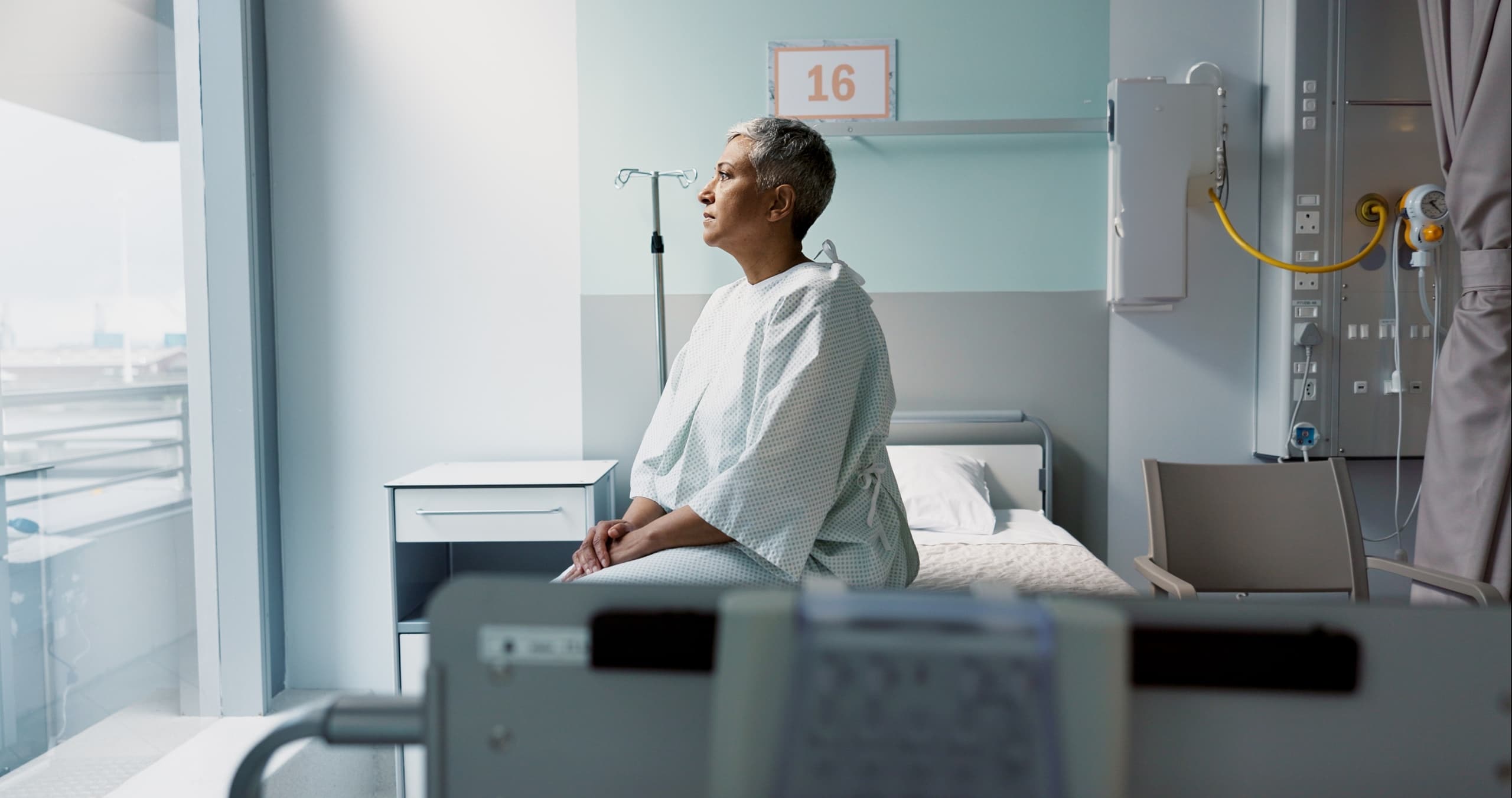 A woman looks out the window sitting on a hospital bed